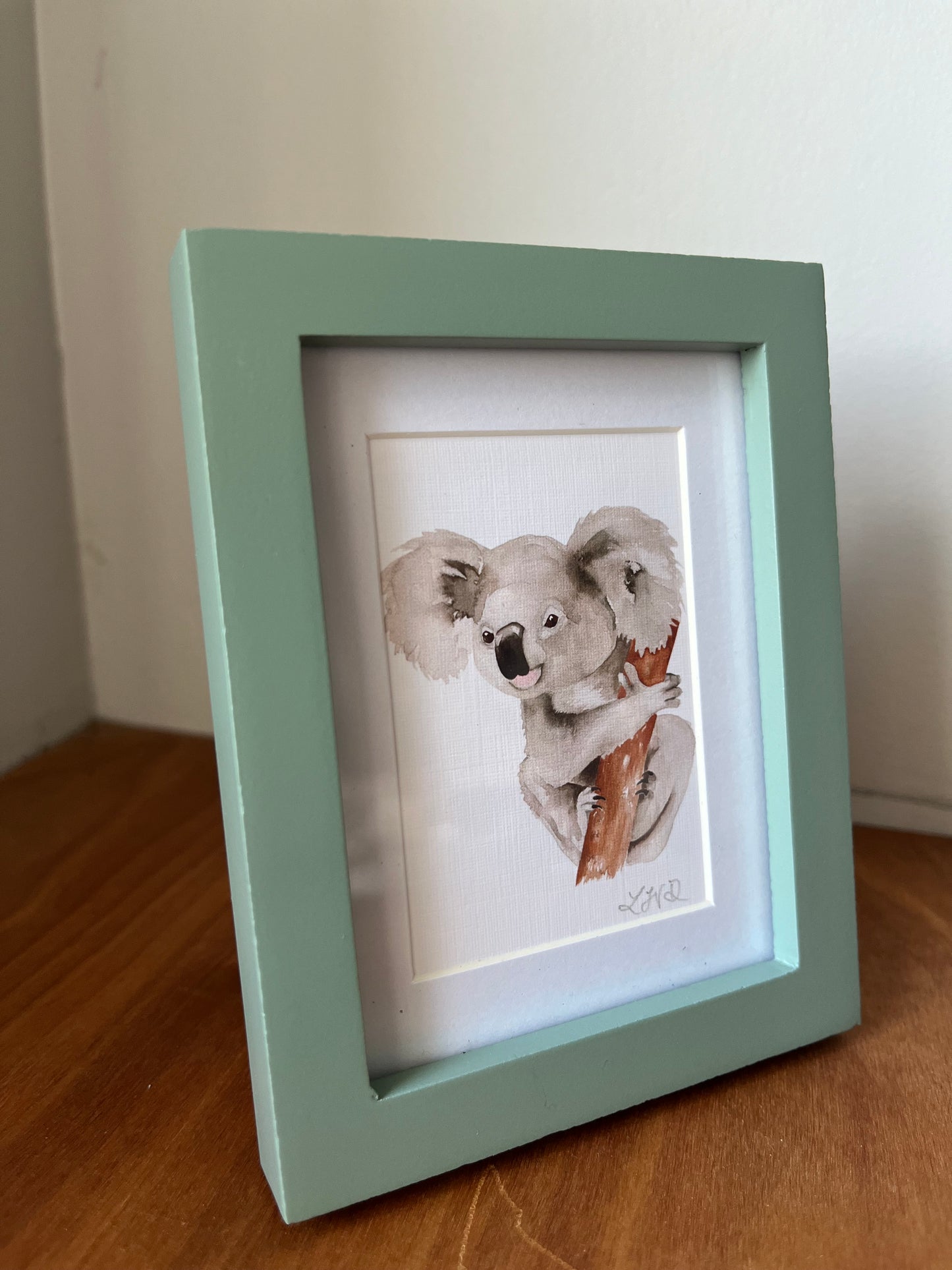 Koala watercolor painting in a small green frame.