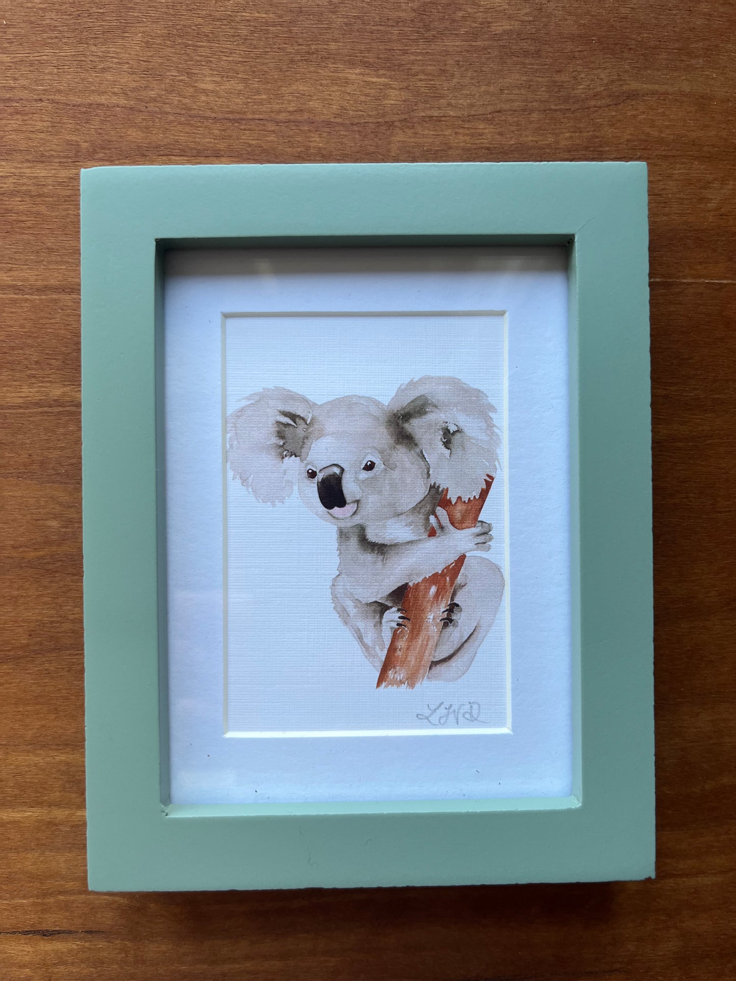 Koala watercolor painting in a small green frame.