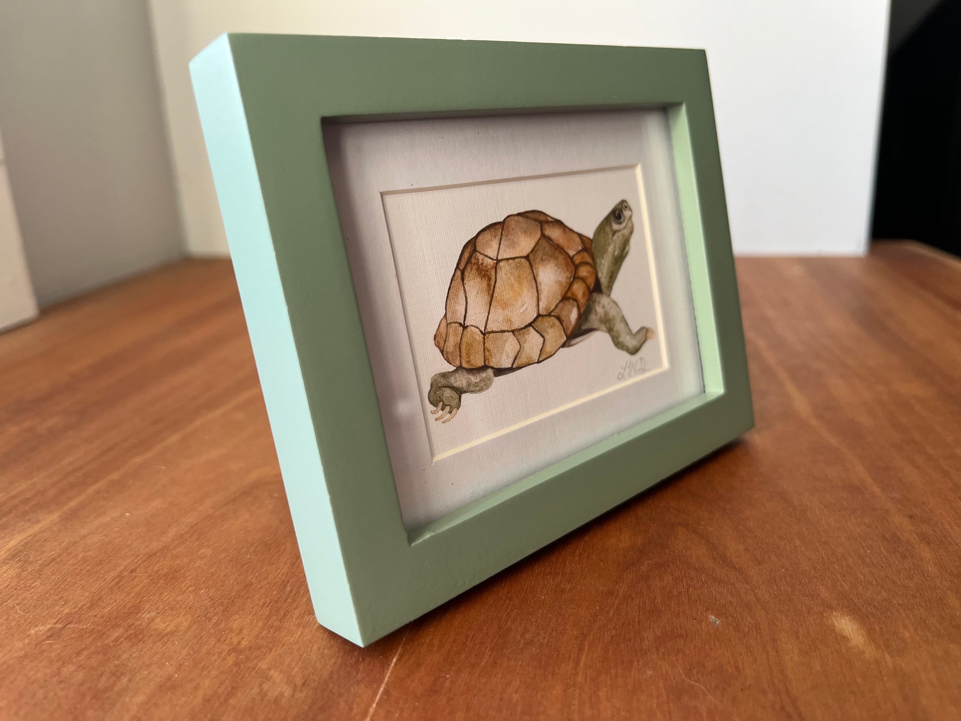 Watercolor turtle in a small green picture frame.