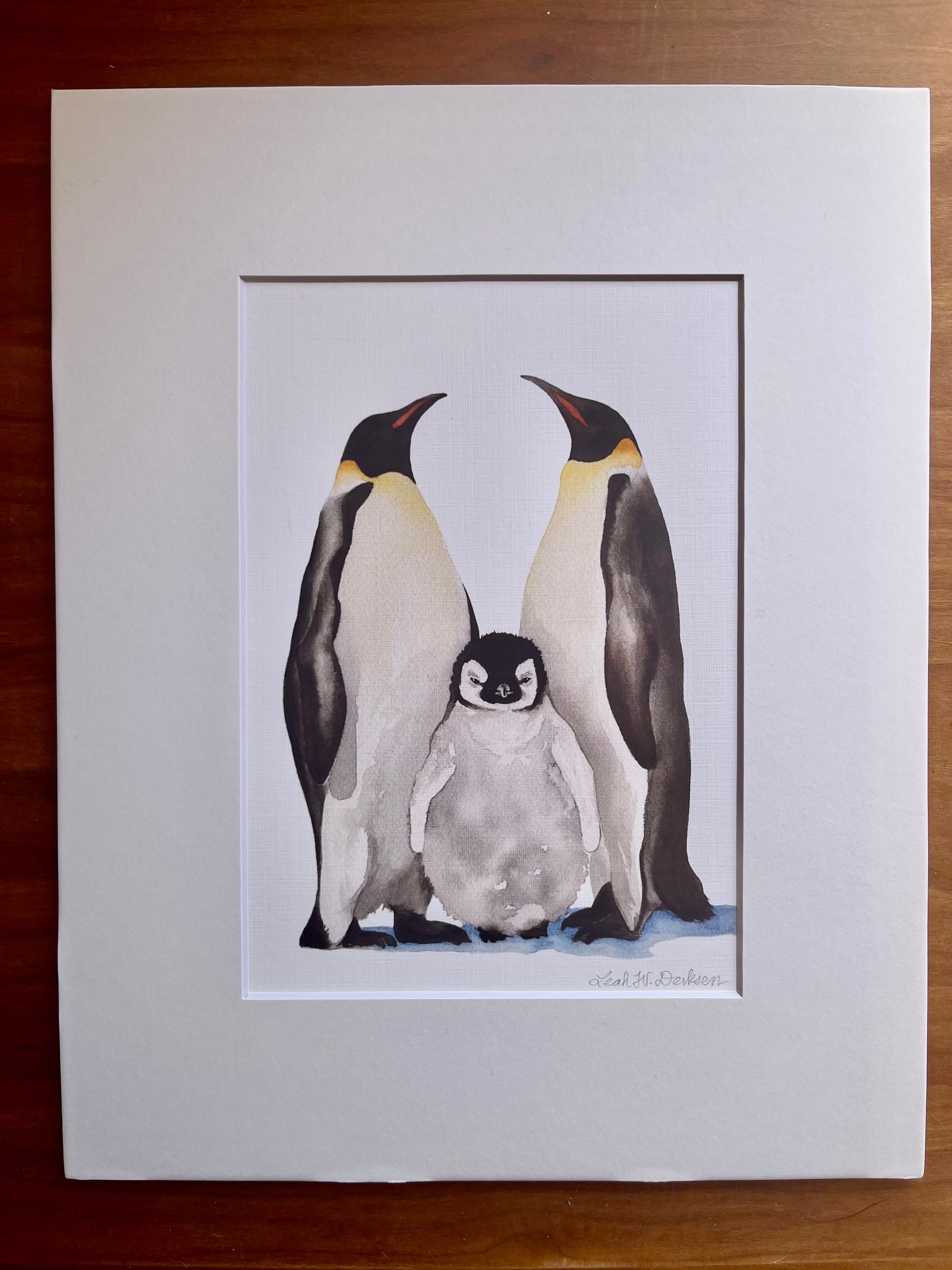 Matted print of a watercolor painting of an emperor penguin family.