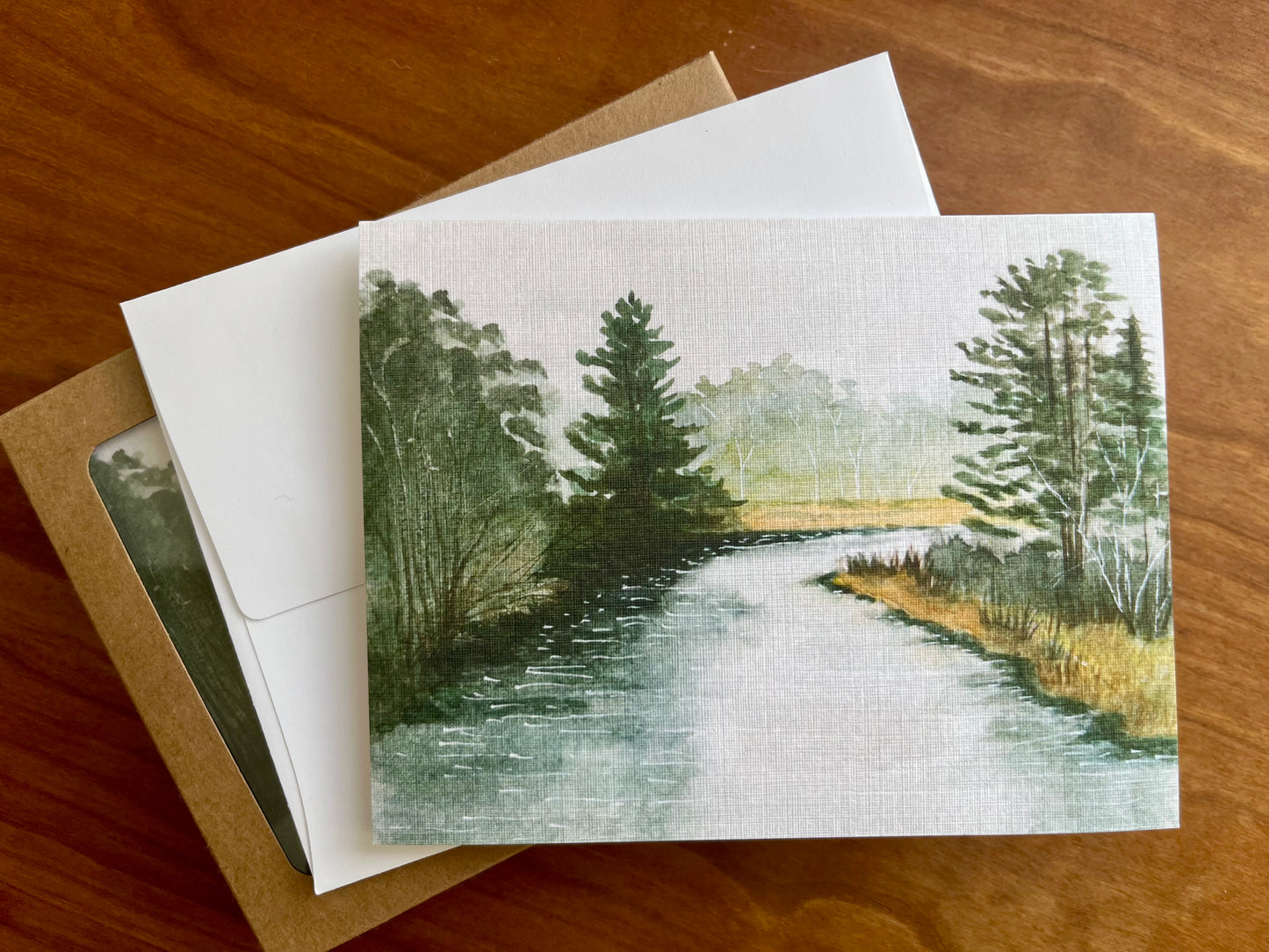 Greeting card with a painting of a Vermont river and forest along with a white envelope.