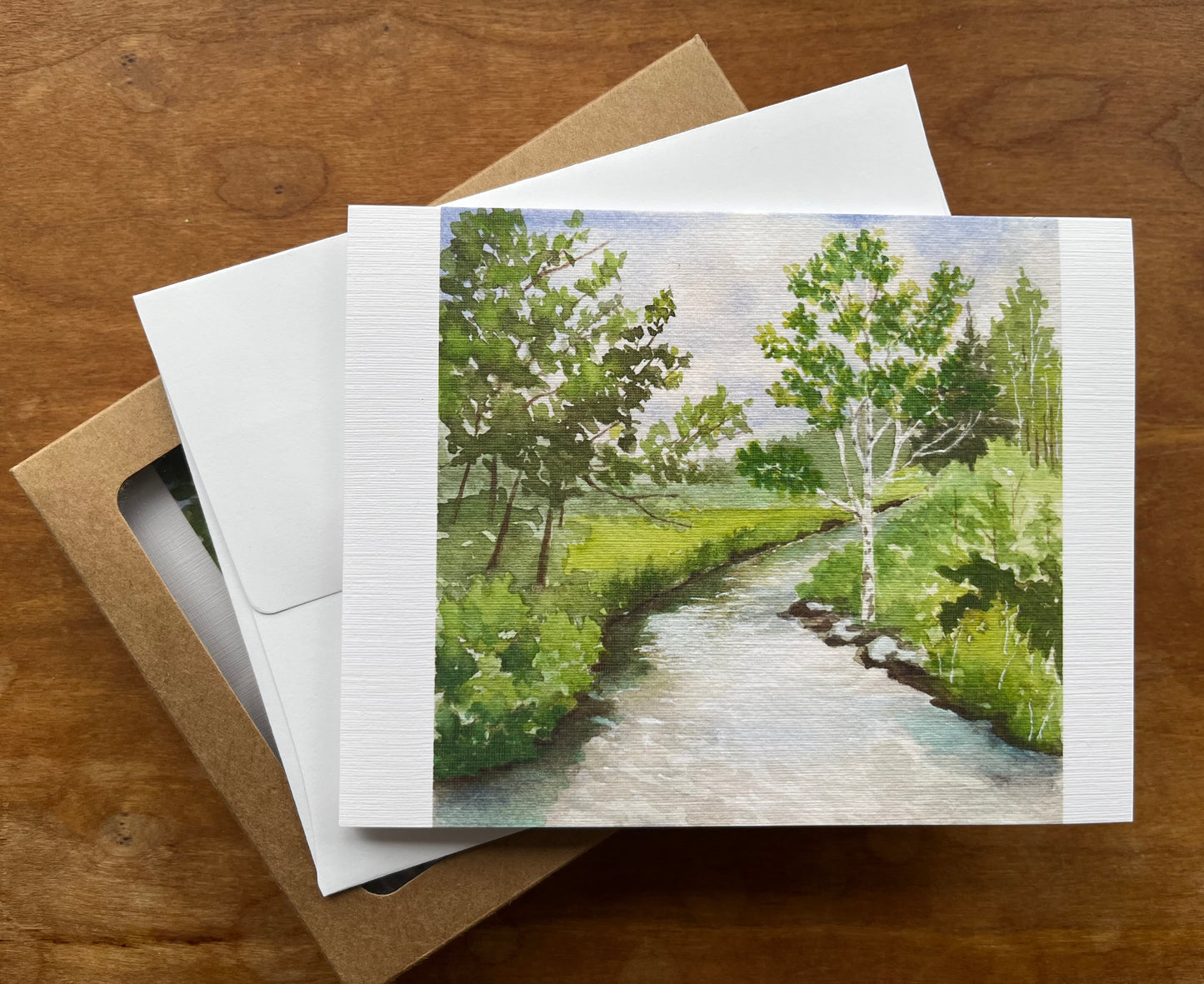 Greeting card with a watercolor painting of a river and trees in springtime.