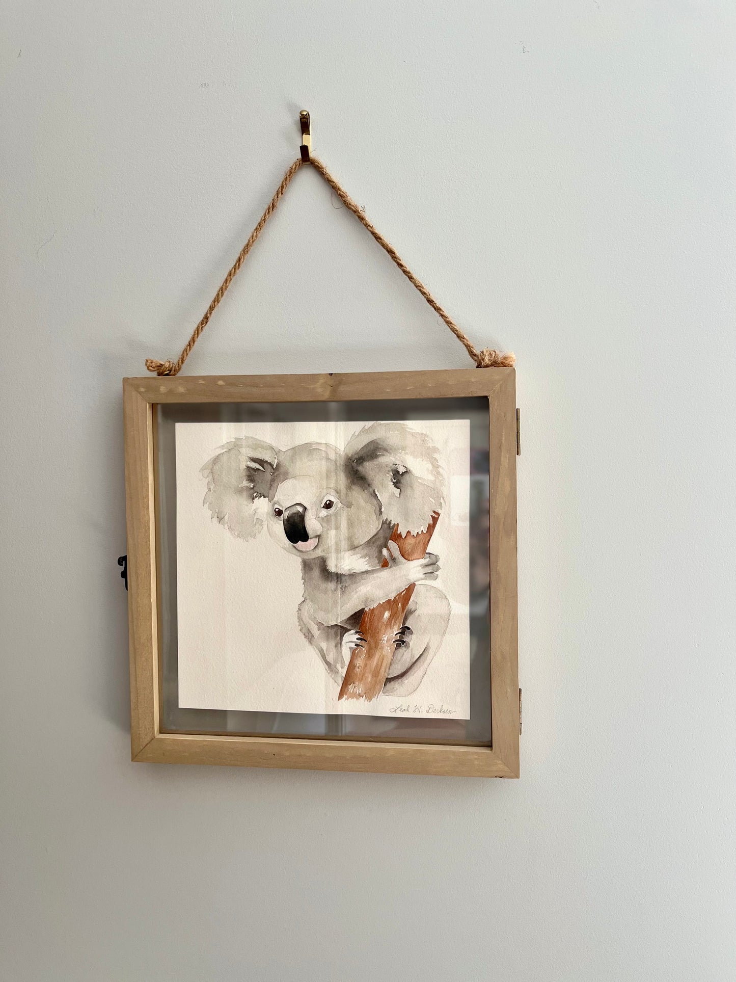 framed watercolor koala painting hanging on a wall.