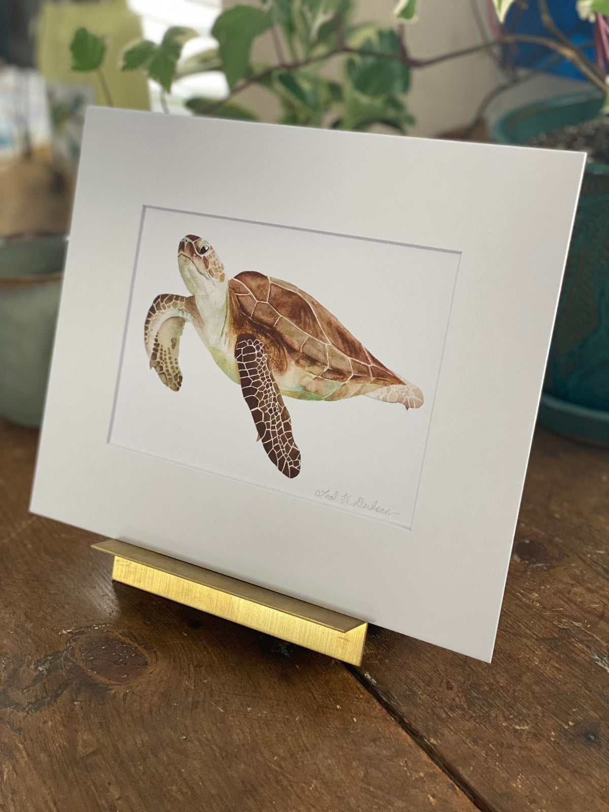 Watercolor print of a sea turtle matted in a gold picture stand. 