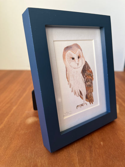 Watercolor painting of a barn owl in a small blue frame. 