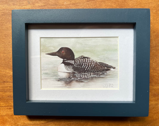 Watercolor painting of a loon in a blue picture frame.