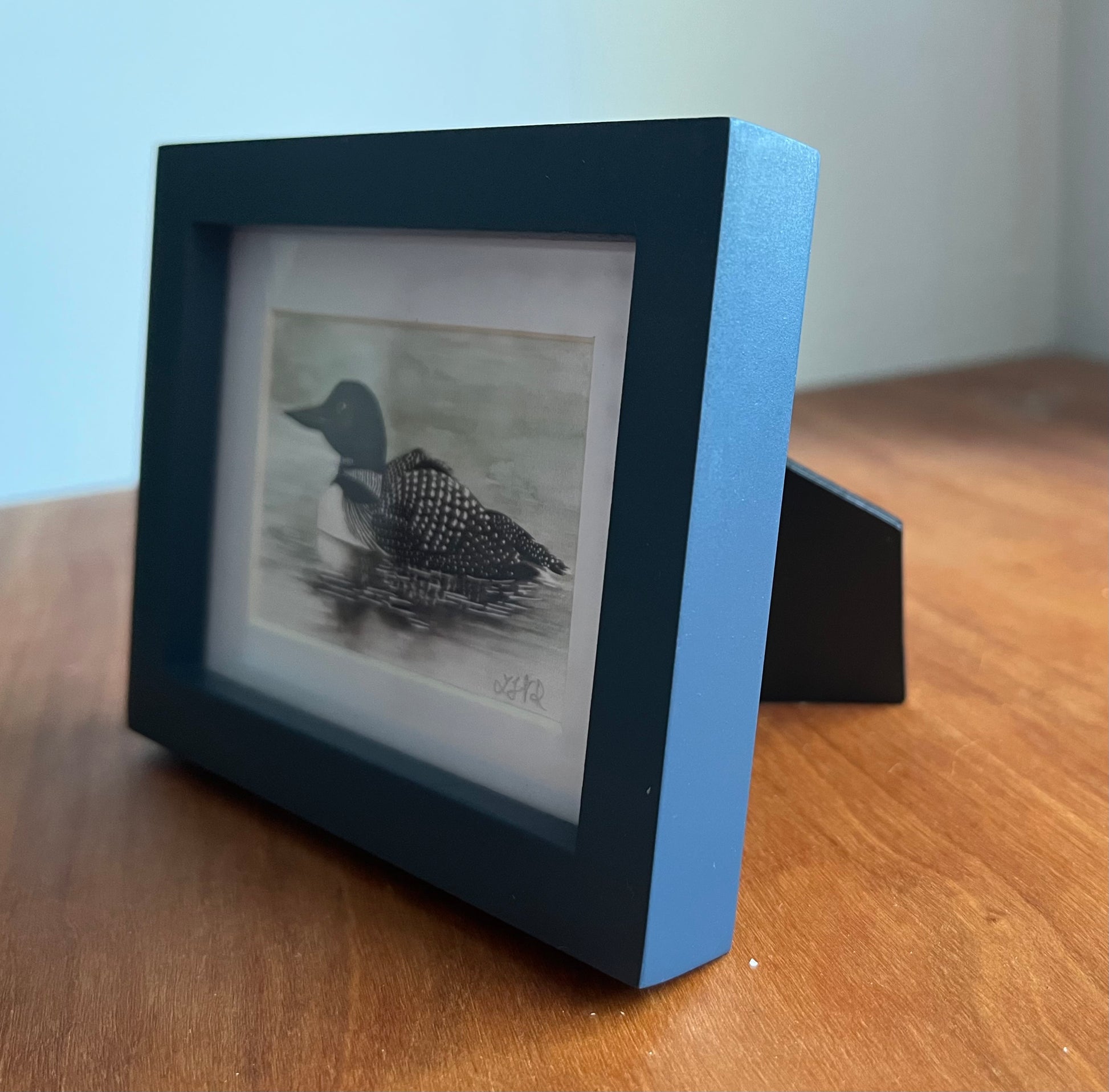 Watercolor painting of a loon in a blue picture frame sitting on an angle.