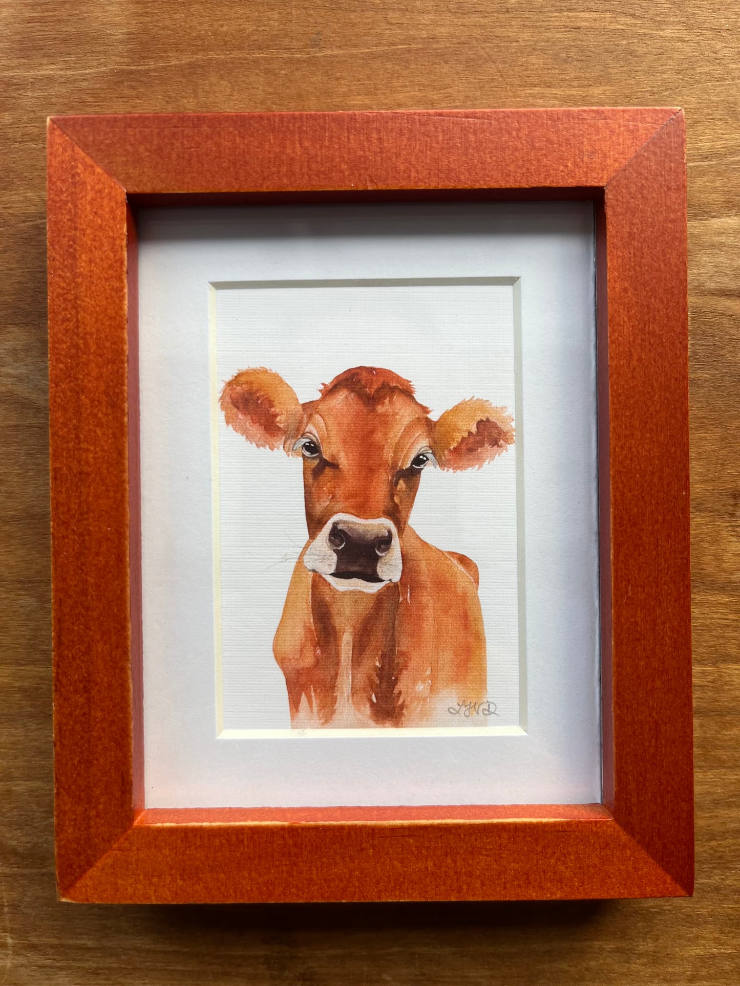 Watercolor painting of a jersey cow in a brown picture frame. 