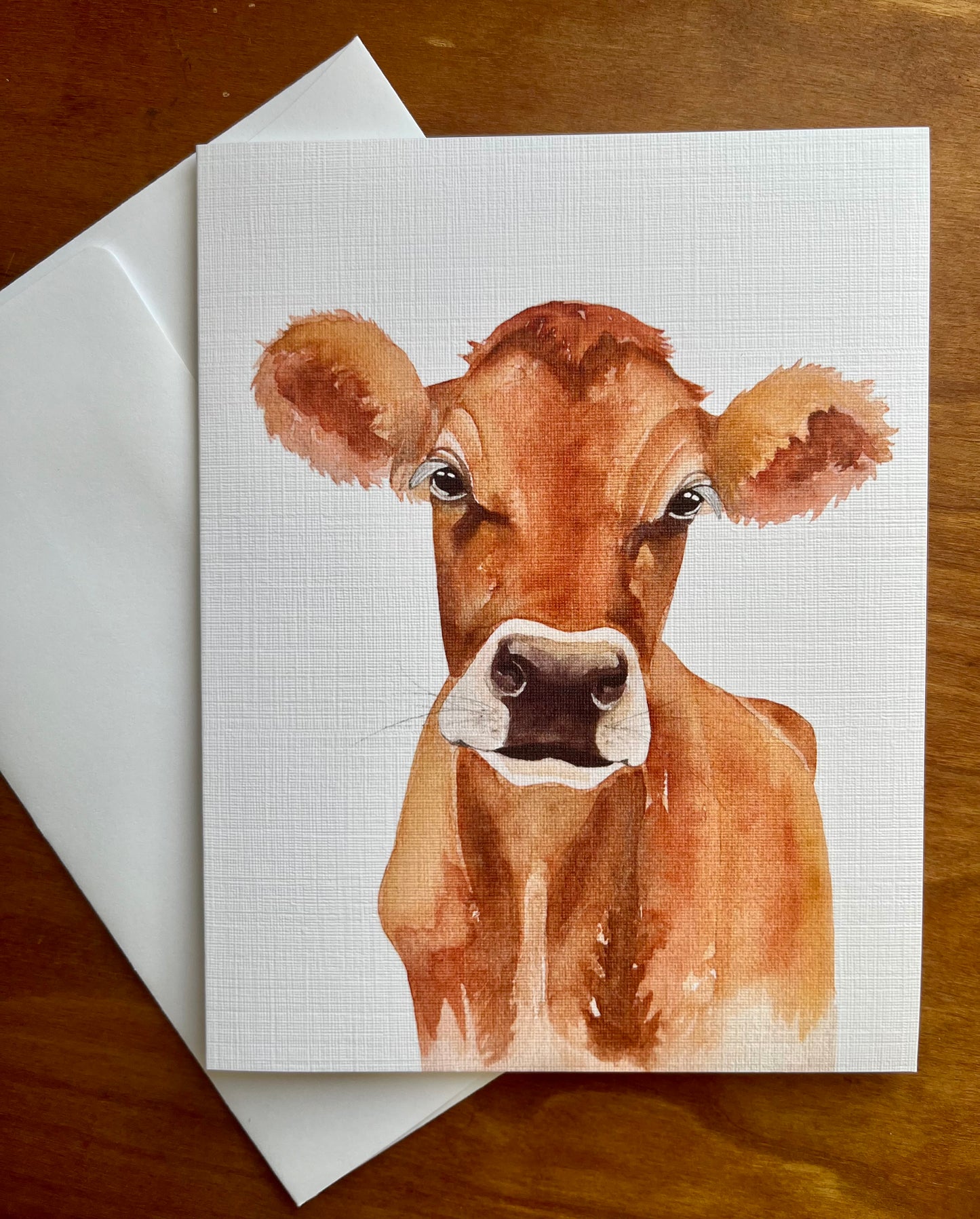 Watercolor painting of a jersey cow printed on a greeting card with a white envelope. 