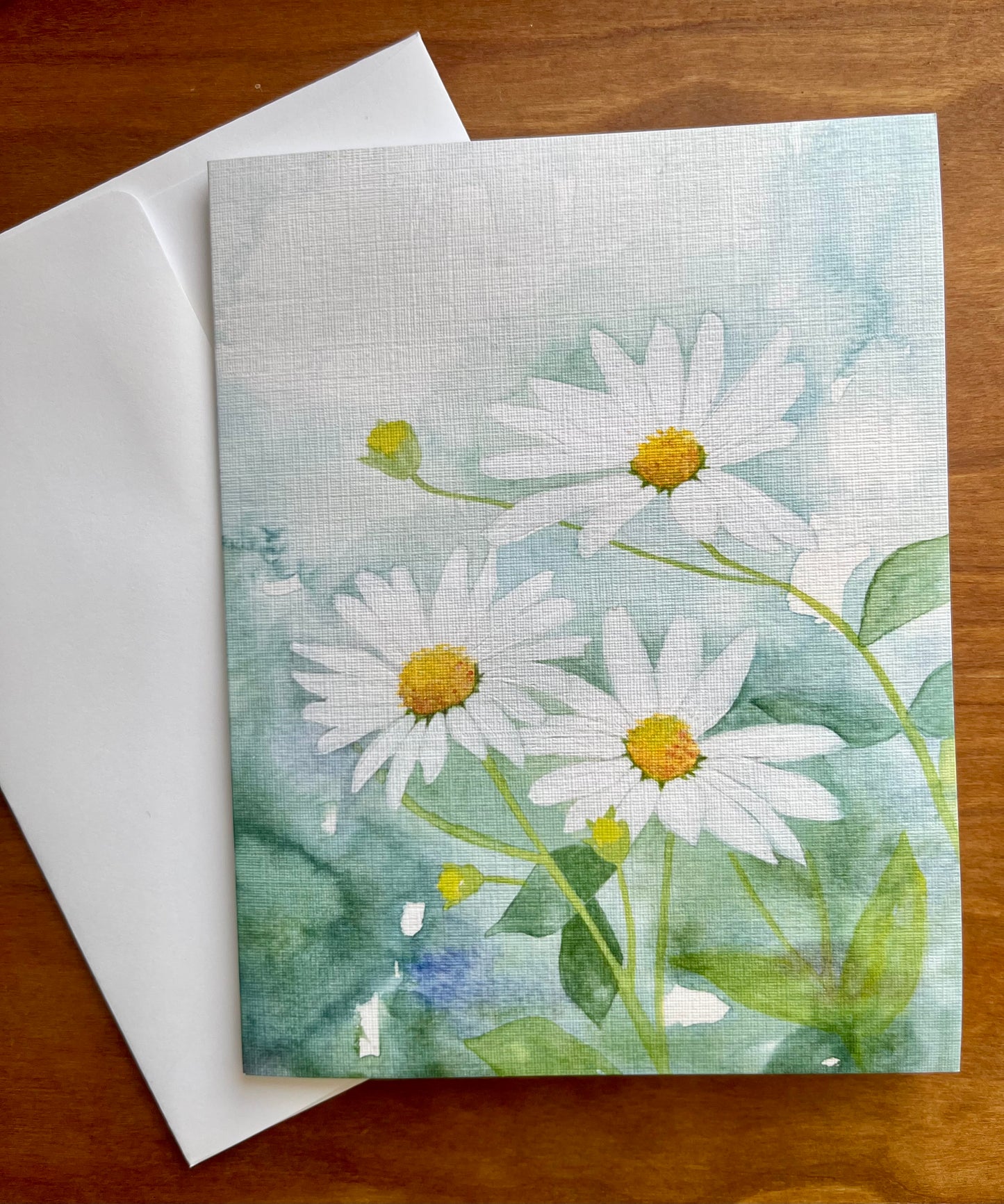 Watercolor daisies painted on a greeting card with a white envelope. 