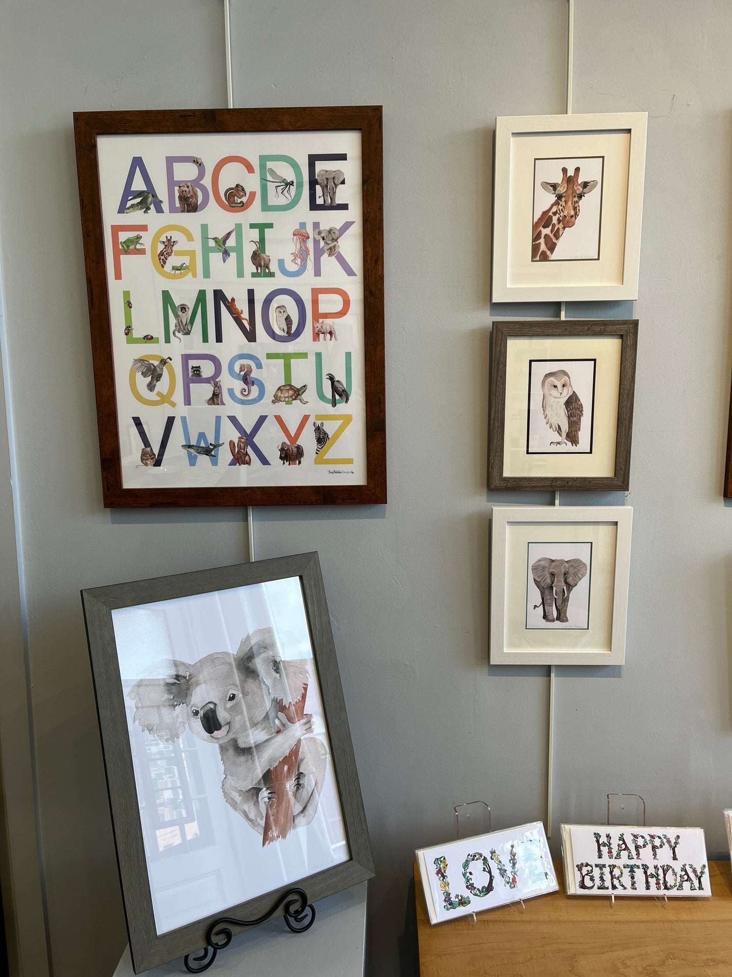 Poster of an animal alphabet in a brown poster frame hanging on a gallery wall. 