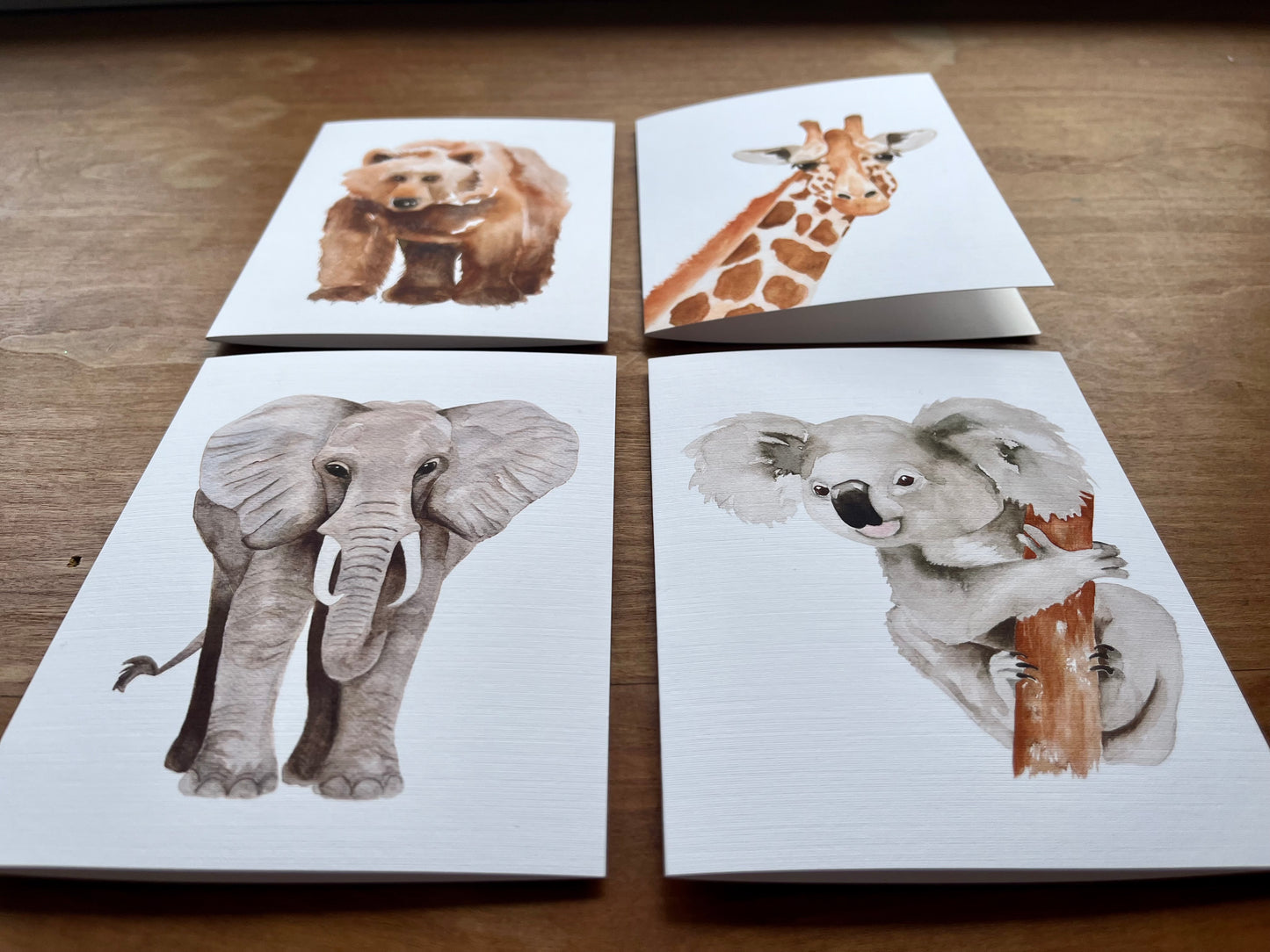 a set of four greeting cards one each of a watercolor bear, giraffe, elephant, and koala.