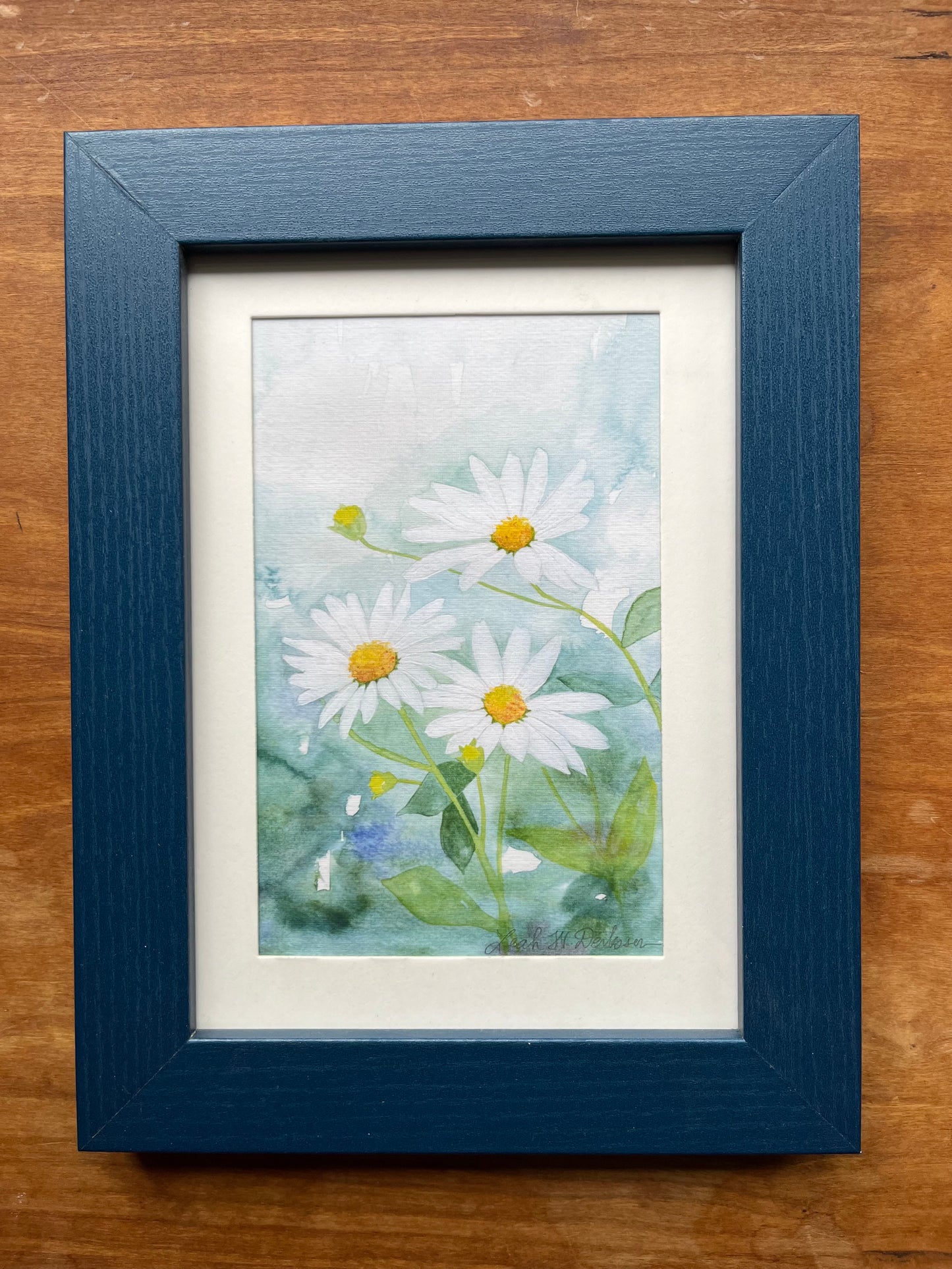 Watercolor daisies in a blue wood picture frame. 