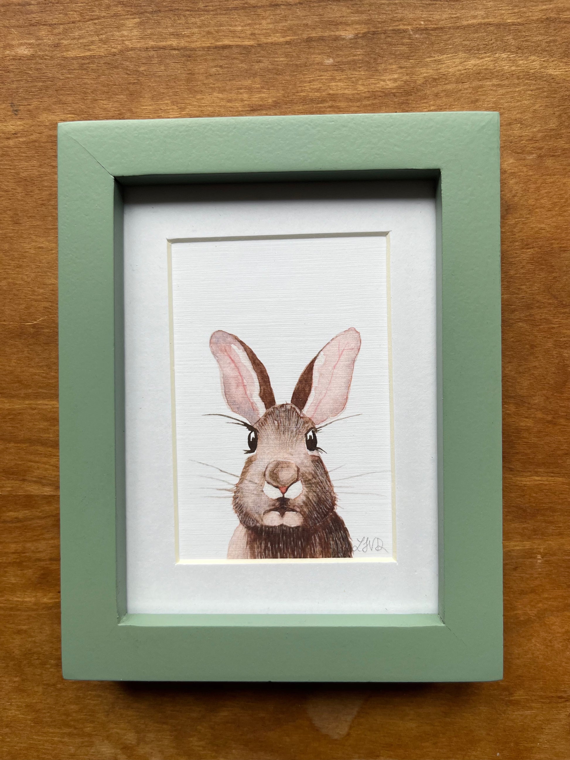 Watercolor rabbit in a green picture frame with a white matte. 