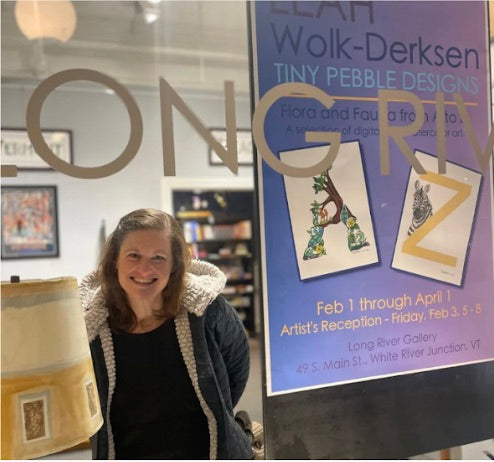 A woman looking out a store window, smiling, with poster of her art in the window.